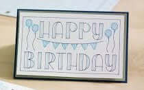 Framed artwork with 'Happy Birthday' text and balloons on a wooden surface