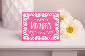 Pink 'Happy Mother's Day' card on a white surface with a white candle and white flowers.